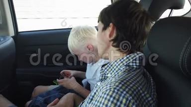 父亲和儿子坐在汽车座椅上玩智能手机，而坐在后座上开车